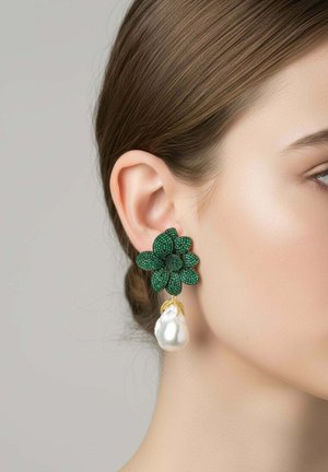 Női fül, zöld virágos patent fülbevalóval, amelyből egy nagy fehér gyöngy lóg, semleges háttér előtt.