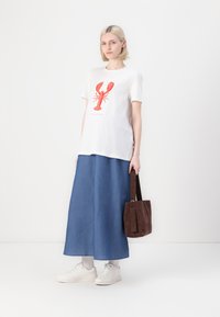 Camiseta blanca con gráfico de langosta roja, combinada con una falda larga azul. Los accesorios incluyen un bolso marrón y zapatillas blancas. Diseño minimalista.