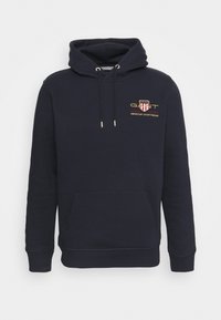 Sudadera azul marino hecha de material suave, con un bolsillo frontal, capucha con cordón y un logo bordado en oro con acentos rojos.