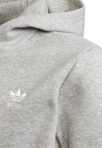 Sudadera con capucha gris de tela suave y texturizada. Presenta un pequeño logo bordado en blanco en el pecho. Diseño simple y funcional.