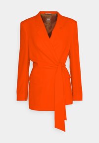 Blazer orange vif à manches longues avec ceinture nouée à la taille et deux poches à rabat sur le devant, présenté sur fond blanc.
