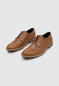 Chaussures de ville en cuir marron avec une finition lisse, fermeture à lacets, bout légèrement pointu et semelle blanche contrastante.