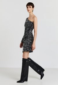 Abito nero decorato con paillettes, spallina unica, abbinato a stivali in pelle nera al ginocchio con buckle e punta a punta.