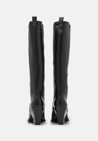 Czarne skórzane kozaki za kolano o dopasowanym kroju, z teksturowanym wykończeniem i wysokimi, kanciastymi obcasami. Posiadają tylne uchwyty, które ułatwiają zakładanie.