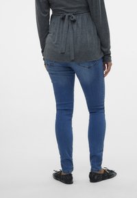 Grå långärmad topp med knyt vid midjan, matchad med blå tajta jeans. Svarta ballerinas fulländar outfiten och betonar den avslappnade stilen.