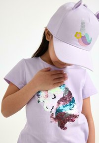 Lavendel t-shirt med en flerfärgad paljett-unicorn-design, tillsammans med en matchande lavendelkeps med en unicornhorn och blommiga detaljer.