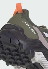 But sportowy w kolorze oliwkowej zieleni z teksturowaną cholewką z siateczki, pomarańczową pętlą do zakładania oraz solidną czarną podeszwą zewnętrzną z sześciokątnym wzorem bieżnika.