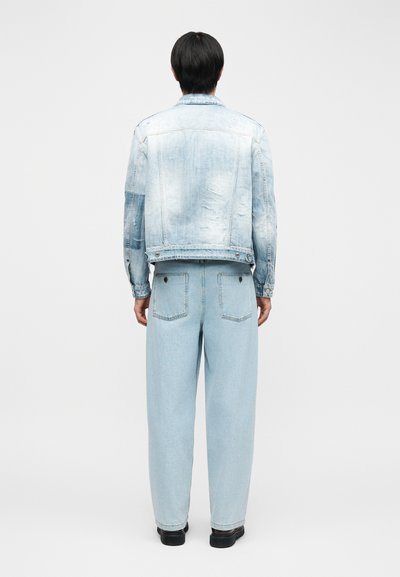 Άτομο που στέκεται με την πλάτη γυρισμένη, φοράει ανοιχτό μπλε τζιν μπουφάν με φθορές και τζιν παντελόνι ψηλόμεσο, φαρδύ στο πόδι, σετ με μαύρα παπούτσια.