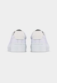 Paire de baskets blanches basses avec des semelles épaisses, des languettes visibles au talon et "Tommy Hilfiger" embossé au dos des semelles.