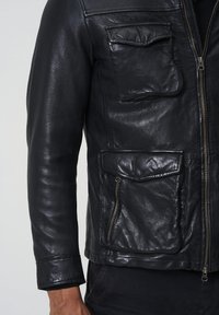 Svart läderjacka med en strukturerad yta. Utrustad med dragkedja fram, två framfickor och en ficka på bröstet. Klassisk design.