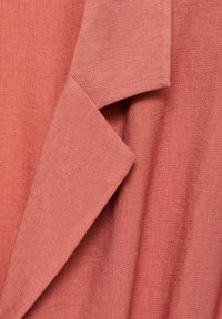 Tessuto color salmone caratterizzato da una trama texture. L'angolo presenta un bordo piegato, indicando un design a strati con una caduta morbida.
