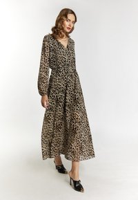 Maxikleid mit Leopardenmuster, langen Ärmeln, tailliertem Schnitt, fließendem Stoff und tiefem V-Ausschnitt, kombiniert mit schwarzen Mules mit goldenen Akzenten.
