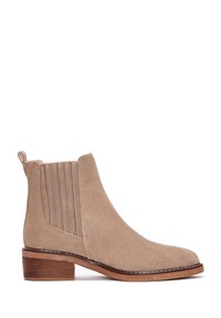 Bottines en suède beige avec des panneaux latéraux élastiques et un talon empilé. Texture lisse avec des coutures contrastantes et un design de bout arrondi.