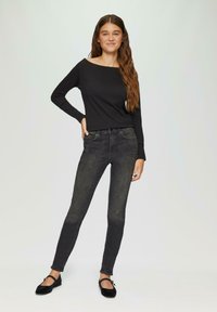 Zwarte lange mouwen top met een brede halslijn, gecombineerd met slim-fit donkergrijze jeans. Zwarte ballerina's met een lage hak en een bandje over de voet.