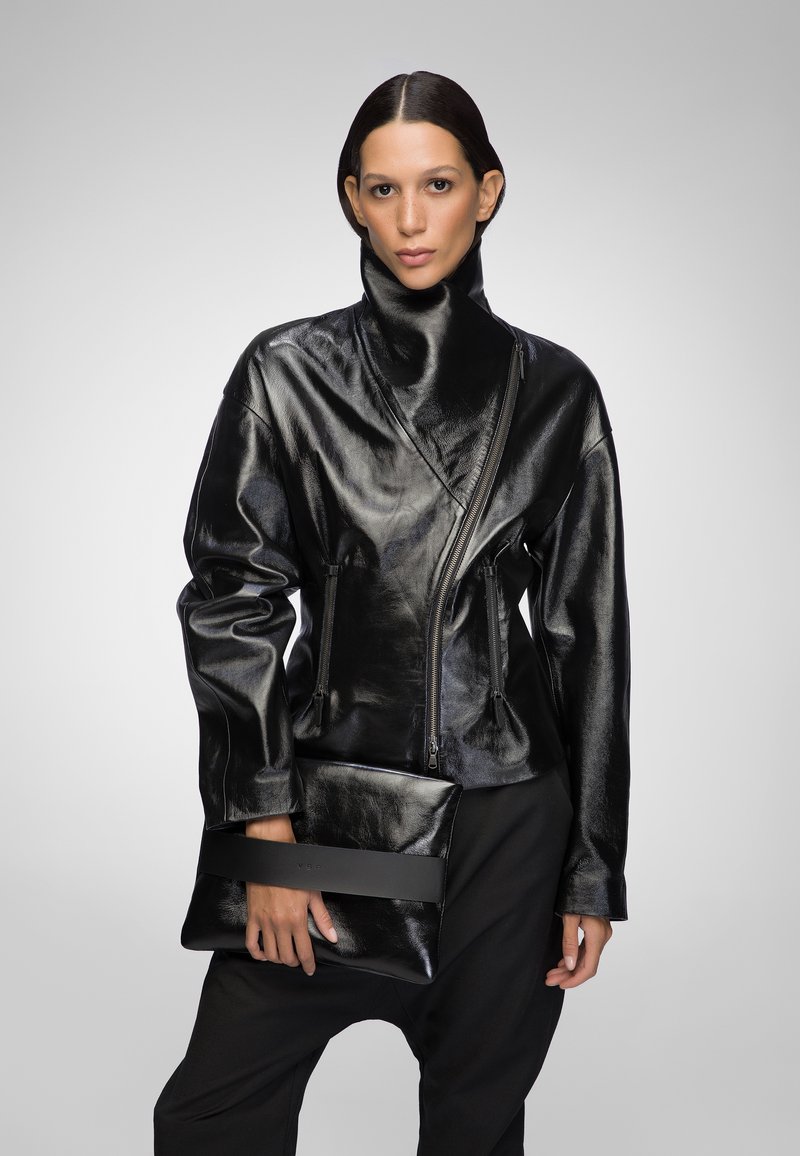 Black leather jacket with a high collar and asymmetrical zip detail; held with a matching black clutch featuring a horizontal strap.