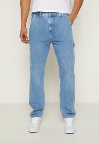 Ljusblå denim cargo-byxor med rak passform, har sidofickor och en urblekt textur, kombinerat med vita sneakers.