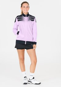 Ljuslila sportjacka med svarta detaljer, dragkedja fram och sportig design. Matchad med svarta shorts och vita sneakers.
