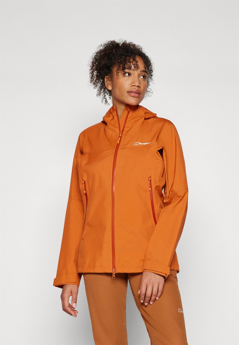 Veste imperméable orange avec capuche, dotée de poches zippées et de fermetures éclair contrastantes. Texture lisse et coupe décontractée.
