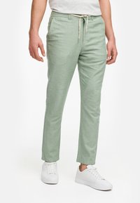 Ljust gröna, avsmalnande byxor i ett mjukt, strukturerat tyg; har en dragsko i midjan och sidofickor; kombineras med vita sneakers.