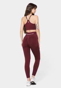 Maroon sports bra with a racerback design, paired with matching high-waisted leggings featuring mesh accents. White logo detail at the waistband.