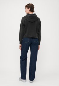 Kuttet svart hettegenser med hette, kombinert med høyt liv mørkeblå rette jeans og lysegrå joggesko.