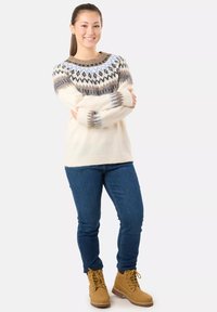 Strickpullover in Creme mit gemustertem Einsatz in Blau, Braun und Schwarz. Kombiniert mit blauen Jeans und hellbraunen Schnürstiefeln.