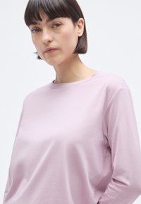 T-shirt à manches longues de couleur violet clair avec un col rond, fabriqué en tissu doux et texturé, présentant une coupe décontractée et des coutures minimales.