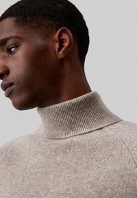 Maglione dolcevita marrone chiaro realizzato in tessuto morbido e strutturato, con collo a coste e design delle spalle senza cuciture.