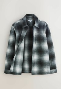 Camicia a quadri in bianco e nero con bottoni sul davanti, colletto e singolo taschino sul petto. Realizzata in tessuto testurizzato con un motivo a gradiente.