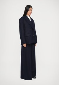 Marineblaues, übergroßes, doppelt-knöpfbares Blazer mit ausgeprägten Revers, flachen Taschen und schwarzen Knöpfen, kombiniert mit weit geschnittenen Hosen.