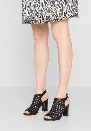 Sandales noires à talons ouverts avec matière tissée, talon bloc solide et bride à la cheville pour un maintien sécurisé.