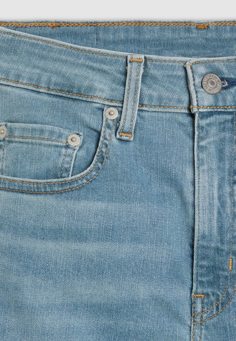 Jeans de denim azul claro con un diseño clásico de cinco bolsillos, costuras en contraste de color naranja y un cierre frontal con botón y remaches metálicos.