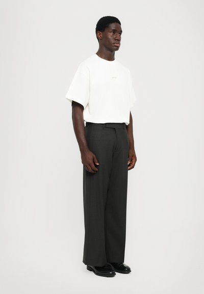 T-shirt bianco a maniche corte con testo "WON", abbinato a pantaloni larghi grigio scuro e scarpe nere. Design semplice e contemporaneo.