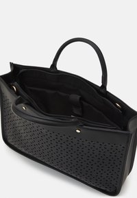 Sort totebag med perforeret frontdesign, to håndtag og indvendige rum inklusive en lynlåslomme.
