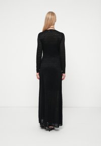 Μαύρο φόρεμα με μακριά μανίκια, που διαθέτει υφή από διάφανο ύφασμα, σχέδιο έως το πάτωμα, πρόσωπο εφαρμοστό και ελαφριά φρενάρισμα από τη μέση.