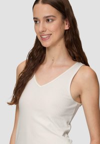 Weißes geripptes Tanktop mit V-Ausschnitt und schmalen Trägern. Weiche Textur mit kontrastierendem Besatz entlang des Ausschnitts.