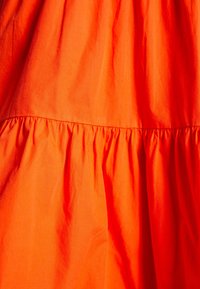 Tissu orange vif avec une couture froncée créant de douces plis et une texture dans le matériau.