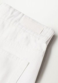 Gros plan d'un tissu en denim blanc montrant une poche arrière et une étiquette rectangulaire cousue près de la taille.
