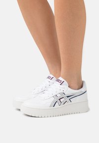 Bílé kožené tenisky s tlustou bílou podrážkou, se stříbrnými a vínovými akcenty, kulatou špičkou a šněrováním v přední části.