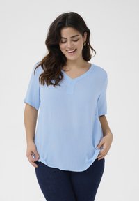 Haut bleu clair à manches courtes avec un décolleté en V et une texture subtile. Présente un ourlet arrondi et une silhouette décontractée. Porté avec un jean foncé.