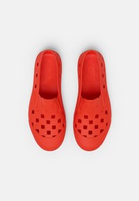 Chaussures en caoutchouc rouges à enfiler, avec des trous de ventilation et une semelle intérieure texturée, dotées d'une finition lisse sans éléments métalliques ou accents visibles.