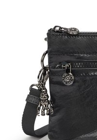 Borsa a tracolla nera in nylon con finitura texture, dotata di una tasca con zip, hardware in argento e un charm pendente. Incluso cinturino regolabile.