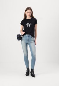 Fekete pamut póló fehér "LOVE" grafikával, elhasználódott kék skinny farmernadrággal és fekete hegyes bokacsizmával párosítva. Kerek táskával kiegészítve.