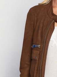 Bruine suede jas met geperforeerde textuur, asymmetrische kraag en zilveren ritsluiting met blauwe hardwareaccenten.