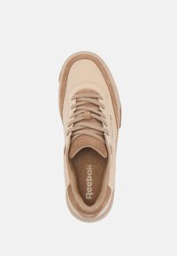 Beige suede and leather sneaker with round toe, textured finish, padded collar, and tonal laces; features Reebok logo on insole.