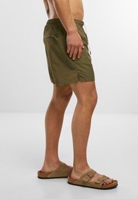 Olívazöld fürdőshorts rugalmas derékkal és zsinórral, oldalsó zsebbel és sima, könnyű anyaggal.