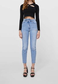 Svart långärmad croptop med ett nyckelhål, kombinerad med ljusblå högmidjade skinny jeans med en slitning och fransad nederkant. Svarta klacksandaler.