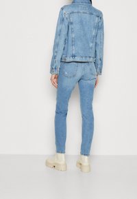 Chaqueta de mezclilla azul claro con diseño clásico y costuras visibles; combinada con jeans azul claro a juego y zapatos de plataforma beige.