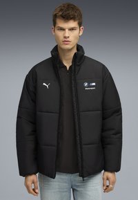 Sort pufferjakke med lynlås foran, polstret design, PUMA-logo på venstre bryst og BMW Motorsport-branding. Blødt materiale, afslappet pasform.