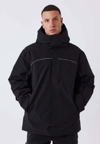 Zwarte waterdichte jas met een hoge kraag, ritssluiting en reflecterende accenten langs de schouders. Heeft een gladde textuur en een oversized pasvorm.